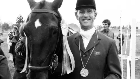 Getty Images Richard Meade standing with his horse. He is wearing a riding hat and jacket with the British flag sewn into his lapel. He has a medal around his neck. 